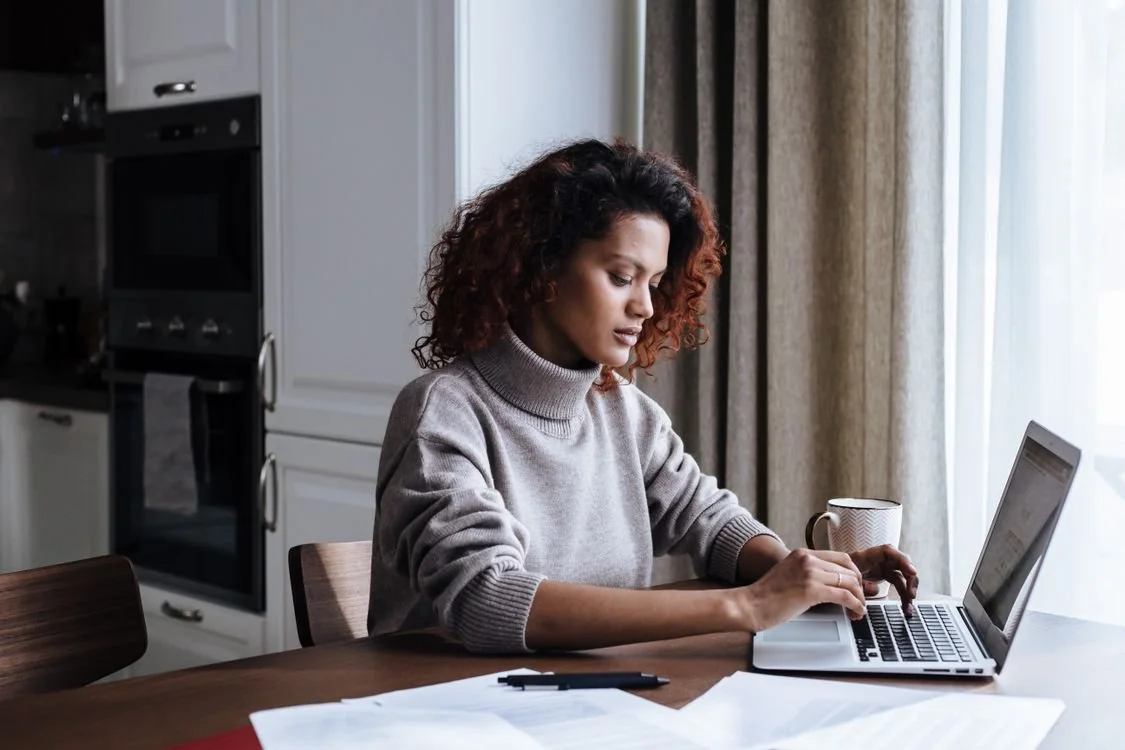 Adult working at a laptop with a notebook at a table