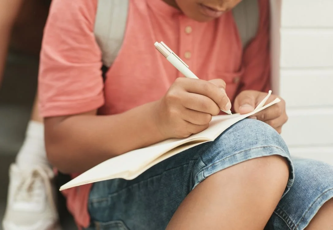 Teen writing in a notebook while reflecting on a situation