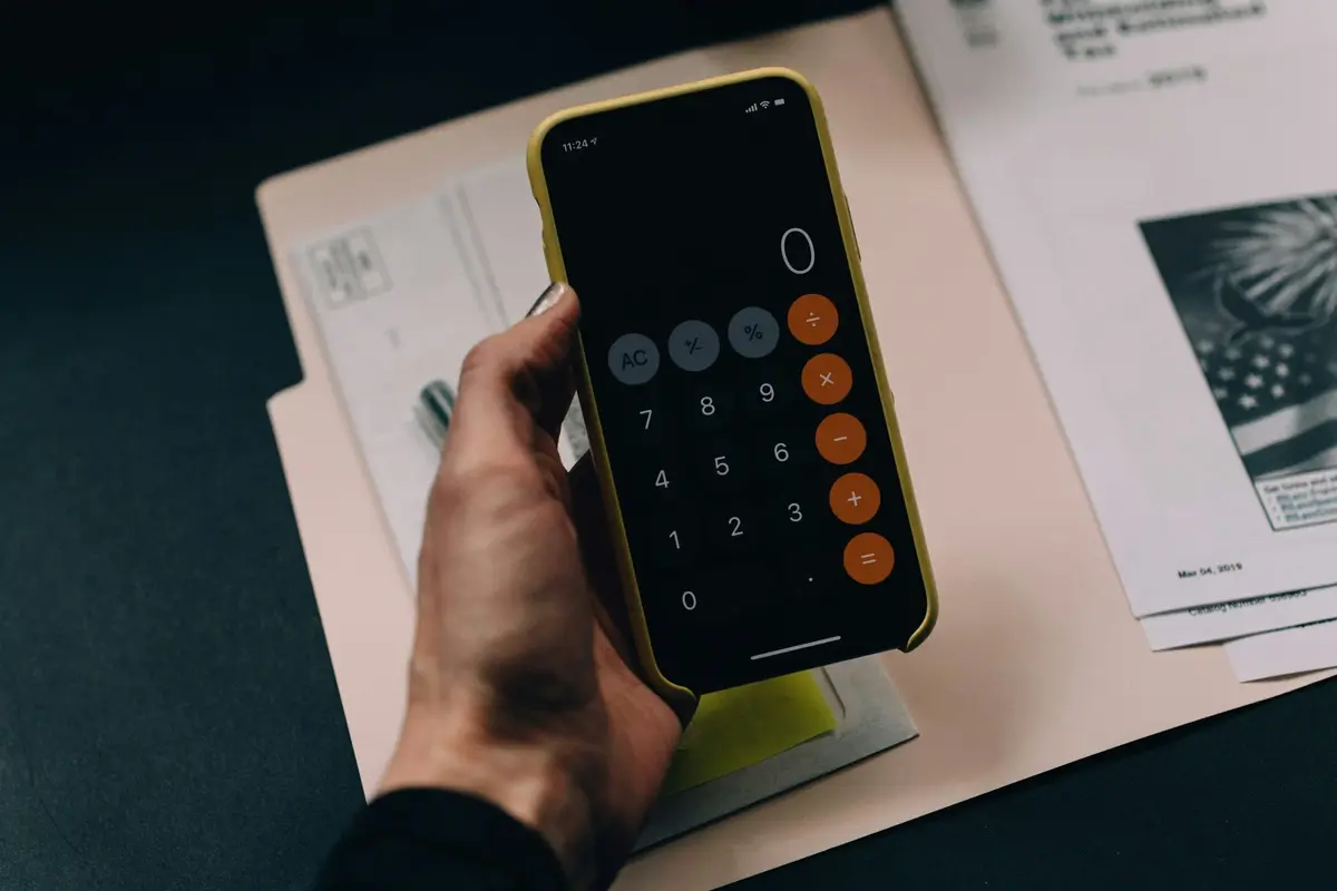 Hand holding a phone calculator over household paperwork