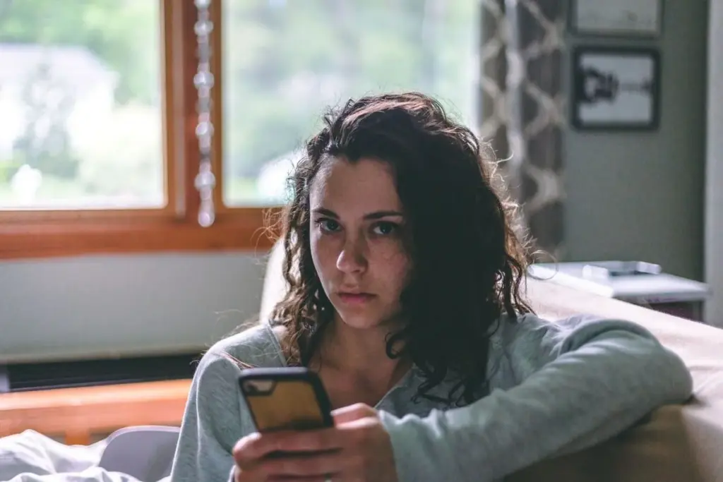 Woman holding a phone while seated on a sofa beside a window