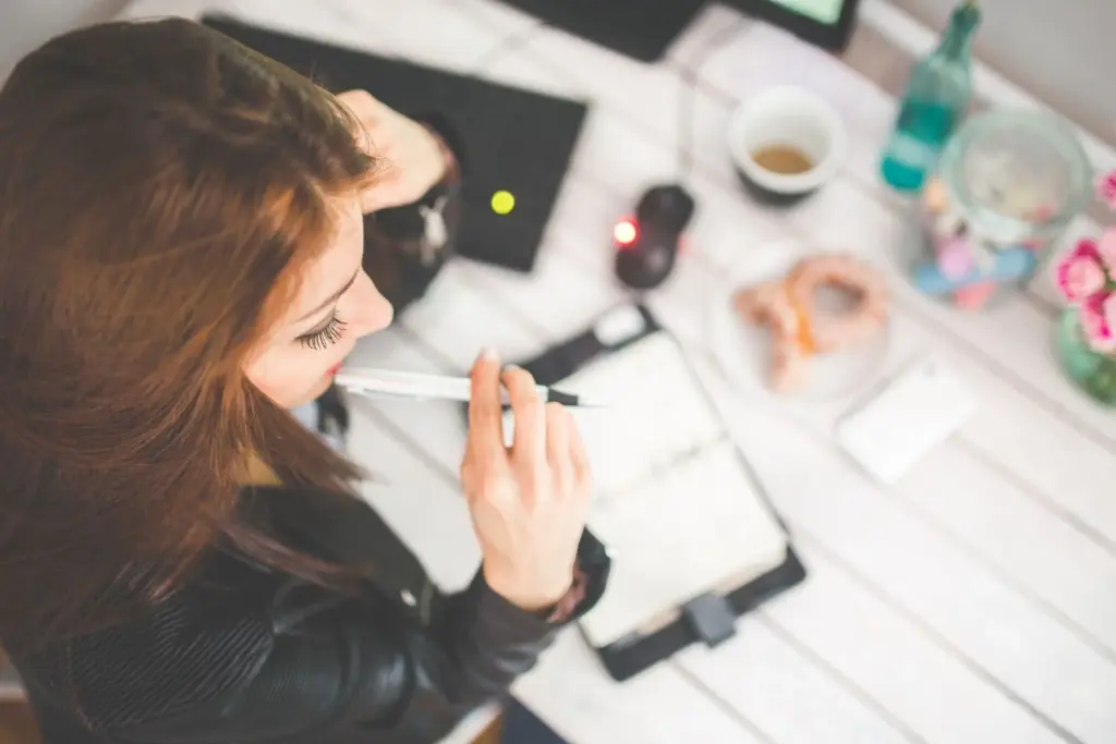A woman pauses with a pen above her notebook at a desk