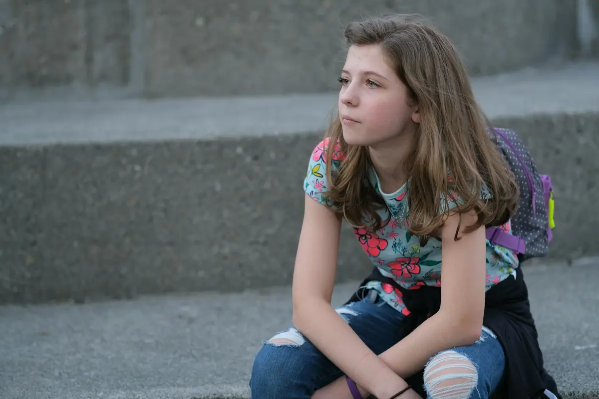 Student with a backpack sitting on outdoor steps, looking to the side