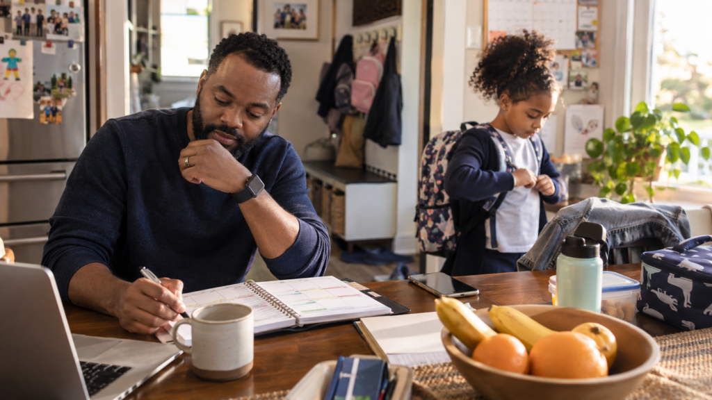Father reviewing a family planner while his child prepares for school