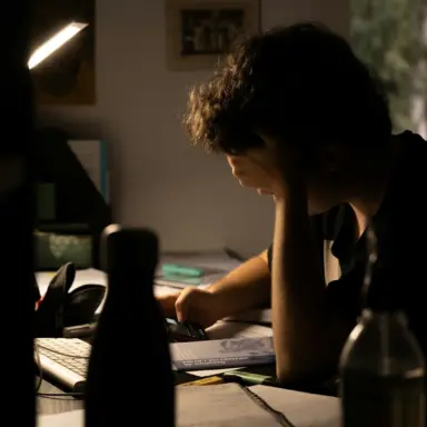 Student seated at a desk reviewing schoolwork in warm natural light