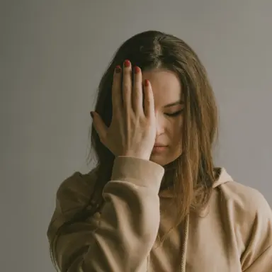 Woman resting one hand against her forehead.