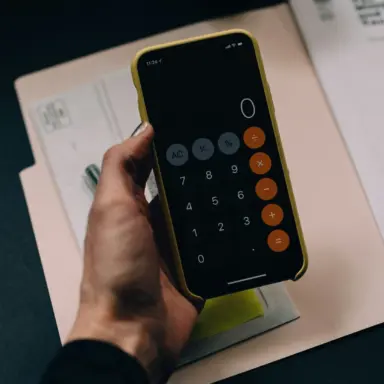 Hand holding a phone calculator above paperwork.