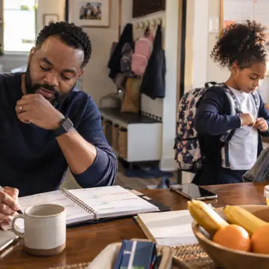 Father reviewing a family planner while his child prepares for school