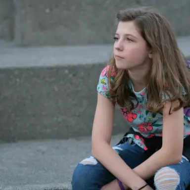Teen sitting on outdoor steps with a backpack.