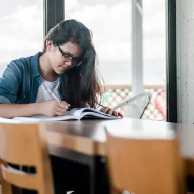 Student writing in an open notebook at a table.