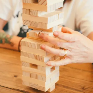 Hands carefully moving a block in a wooden stacking tower.