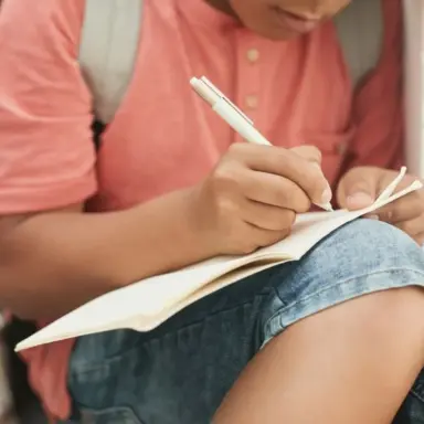 Student writing in a notebook resting on their knee.